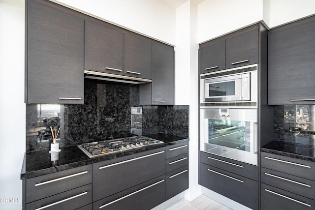 kitchen featuring tasteful backsplash, dark stone counters, dark brown cabinets, exhaust hood, and appliances with stainless steel finishes