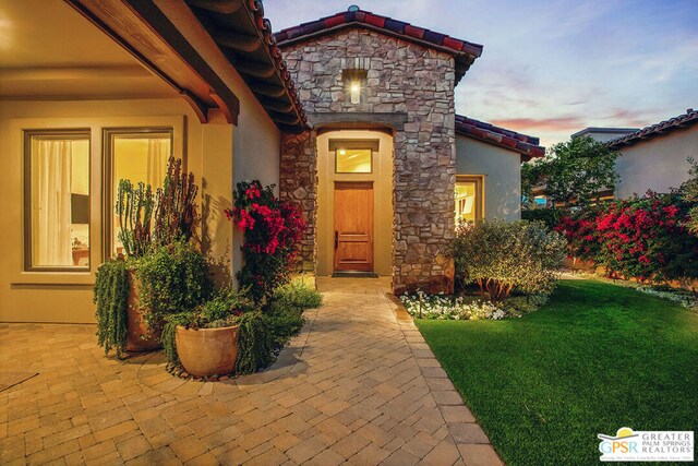 exterior entry at dusk featuring a patio area and a lawn