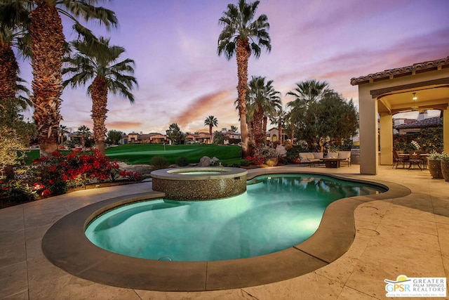 pool at dusk featuring a patio area and an in ground hot tub