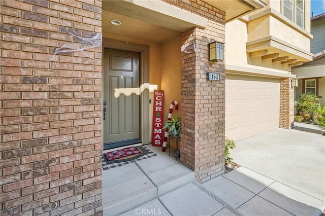 view of exterior entry with brick siding, driveway, and a garage