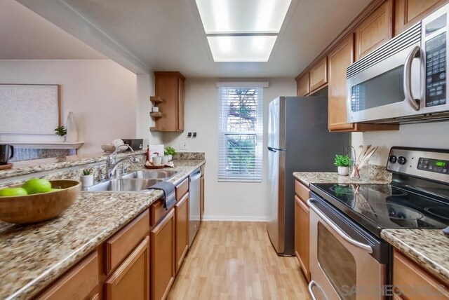 kitchen with light stone countertops, appliances with stainless steel finishes, light wood-type flooring, and sink