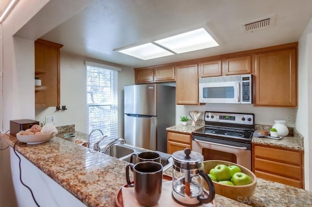 kitchen featuring light stone countertops, appliances with stainless steel finishes, kitchen peninsula, and sink