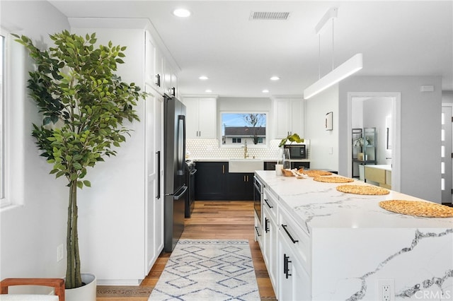 kitchen featuring decorative backsplash, stainless steel fridge, white cabinetry, and an island with sink