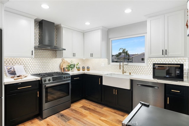 kitchen featuring appliances with stainless steel finishes, wall chimney exhaust hood, sink, white cabinets, and light hardwood / wood-style floors