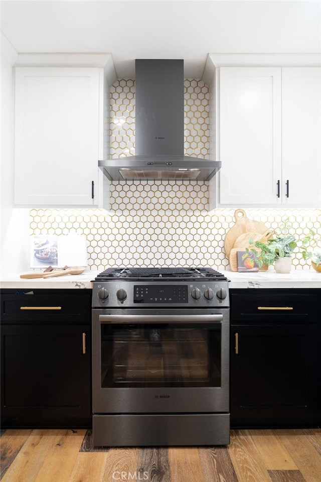 kitchen with white cabinetry, high end stainless steel range, wall chimney range hood, and light wood-type flooring