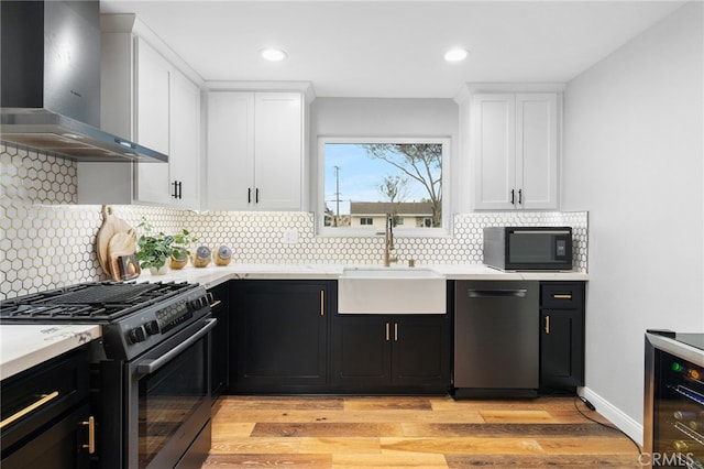 kitchen with white cabinetry, sink, wall chimney range hood, appliances with stainless steel finishes, and light wood-type flooring