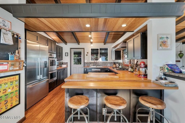 kitchen with beam ceiling, wooden ceiling, stainless steel appliances, kitchen peninsula, and a breakfast bar