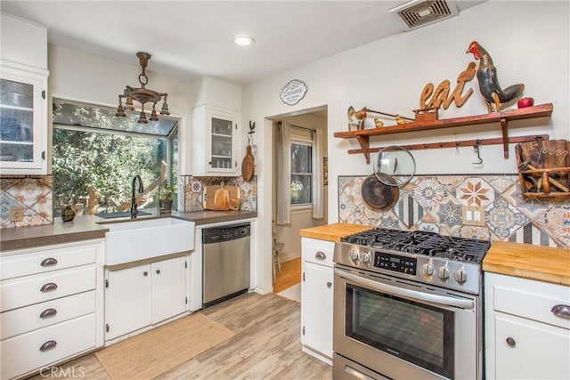 kitchen with appliances with stainless steel finishes, backsplash, sink, white cabinets, and light hardwood / wood-style floors