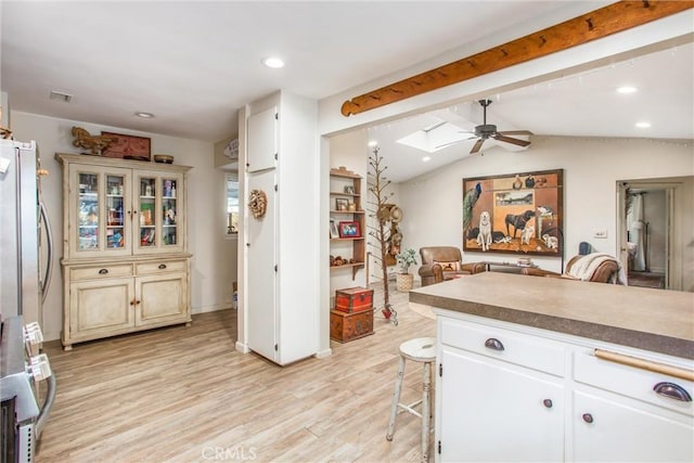 kitchen featuring light hardwood / wood-style flooring, vaulted ceiling with skylight, ceiling fan, a kitchen bar, and stainless steel refrigerator