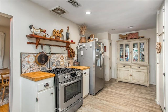 kitchen with tasteful backsplash, butcher block counters, light wood-type flooring, and appliances with stainless steel finishes