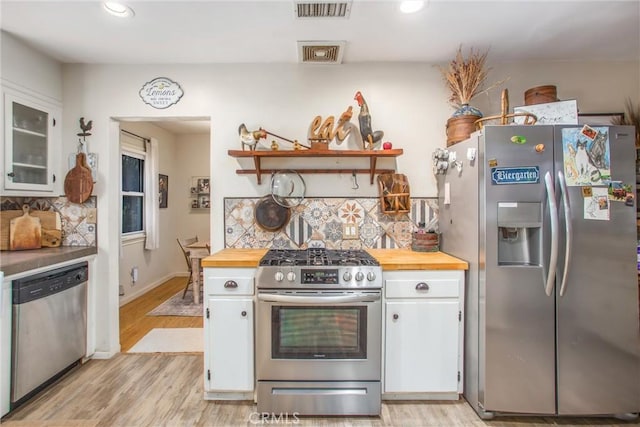 kitchen with butcher block counters, white cabinets, light wood-type flooring, and appliances with stainless steel finishes