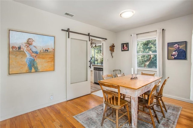 dining space with a barn door, sink, and light hardwood / wood-style flooring