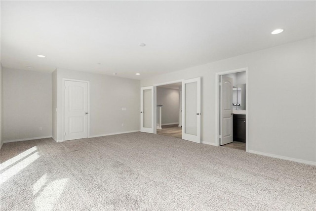 unfurnished bedroom featuring light carpet, french doors, and ensuite bath