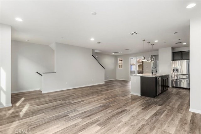 kitchen with a kitchen island with sink, stainless steel appliances, decorative light fixtures, and wood-type flooring