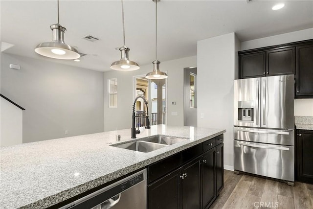 kitchen with light stone countertops, stainless steel appliances, sink, pendant lighting, and light hardwood / wood-style floors