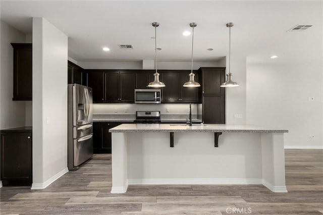 kitchen with light stone countertops, hanging light fixtures, a breakfast bar, appliances with stainless steel finishes, and light wood-type flooring