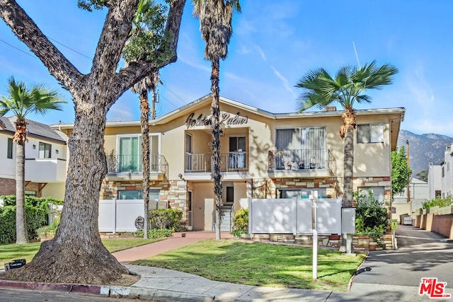 view of front of property with a mountain view, a balcony, and a front lawn