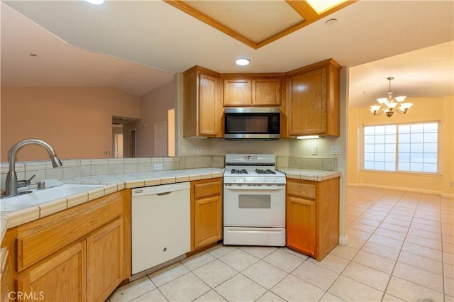 kitchen featuring white appliances, an inviting chandelier, sink, vaulted ceiling, and tile counters