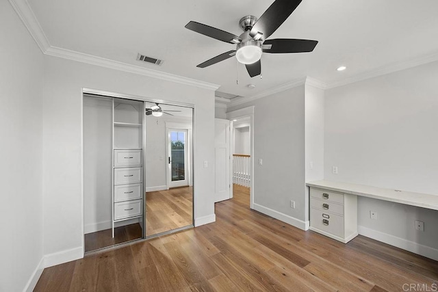 unfurnished bedroom with ceiling fan, a closet, built in desk, and light hardwood / wood-style flooring