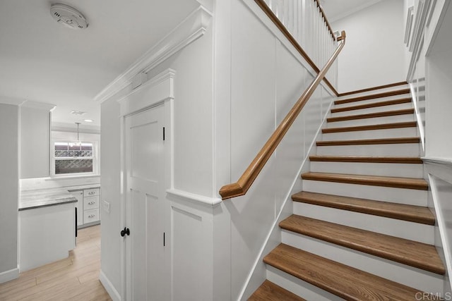 stairway with wood-type flooring, ornamental molding, and an inviting chandelier