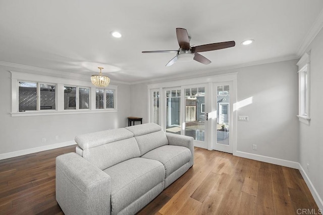 living room with crown molding, a healthy amount of sunlight, ceiling fan with notable chandelier, and hardwood / wood-style flooring