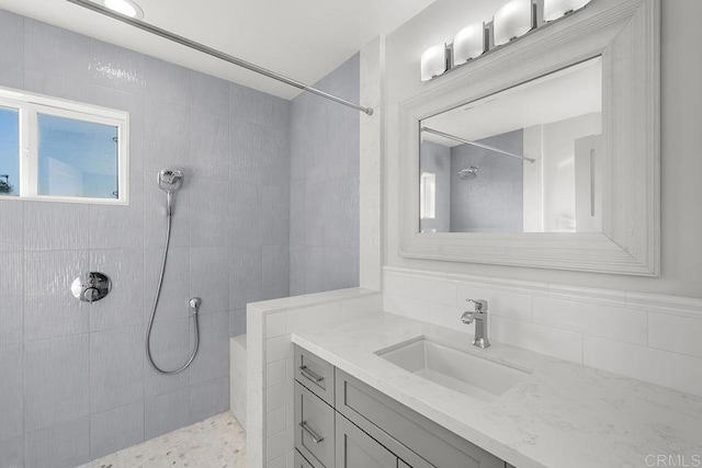 bathroom featuring a tile shower, vanity, and tile walls