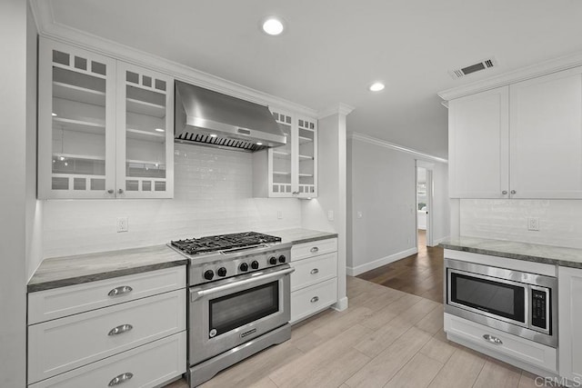 kitchen with white cabinetry, wall chimney range hood, and appliances with stainless steel finishes