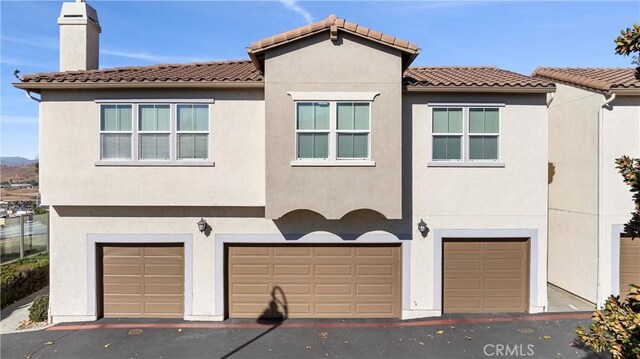 view of front facade featuring an attached garage, stucco siding, a chimney, and a tiled roof