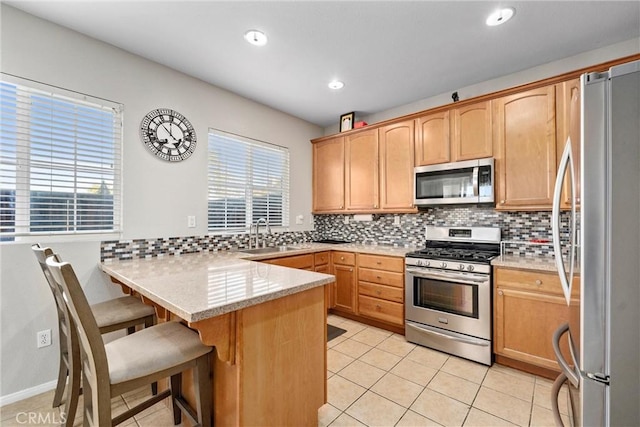 kitchen featuring stainless steel appliances, a peninsula, decorative backsplash, a breakfast bar area, and light tile patterned floors