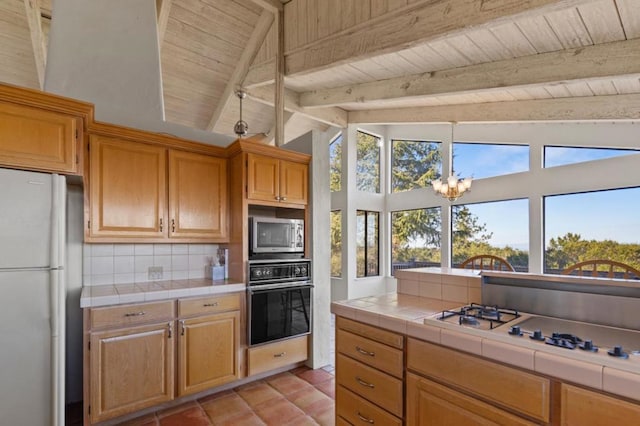 kitchen featuring tasteful backsplash, a notable chandelier, vaulted ceiling with beams, appliances with stainless steel finishes, and tile counters