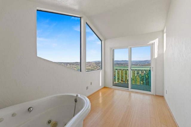 bathroom featuring a tub, vaulted ceiling, a mountain view, and wood-type flooring