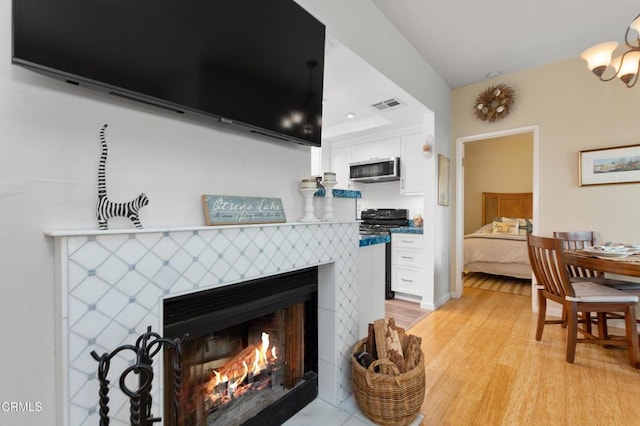 interior space featuring a tiled fireplace, an inviting chandelier, and light wood-type flooring