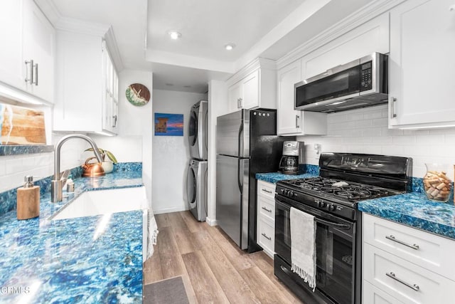 kitchen with light hardwood / wood-style flooring, white cabinets, black appliances, and stacked washer and clothes dryer