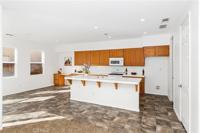 kitchen featuring sink, a kitchen island with sink, a kitchen bar, and white appliances