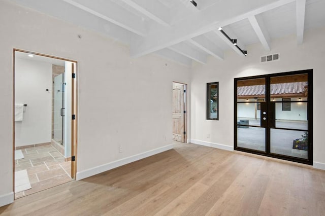 empty room with light hardwood / wood-style flooring and beamed ceiling