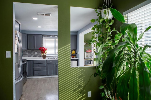 kitchen featuring backsplash, appliances with stainless steel finishes, gray cabinetry, and light hardwood / wood-style floors