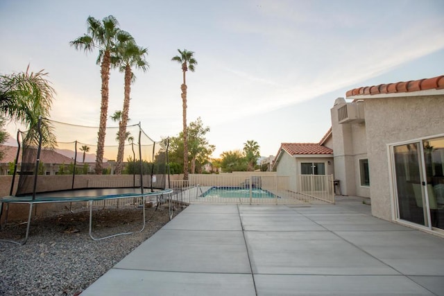 pool at dusk with a patio and a trampoline