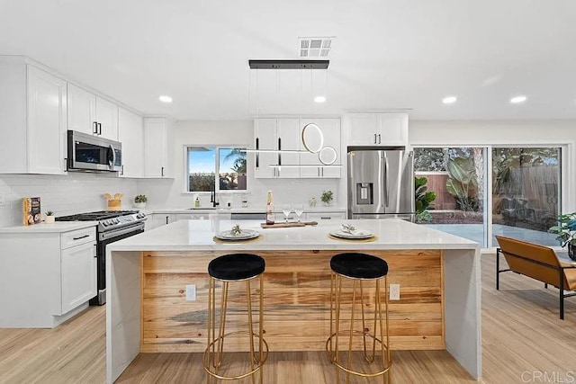 kitchen with a breakfast bar, light wood-type flooring, appliances with stainless steel finishes, a kitchen island, and white cabinetry