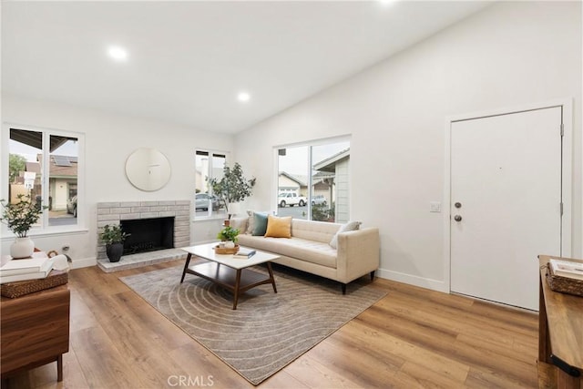 living room with a fireplace, high vaulted ceiling, and light wood-type flooring