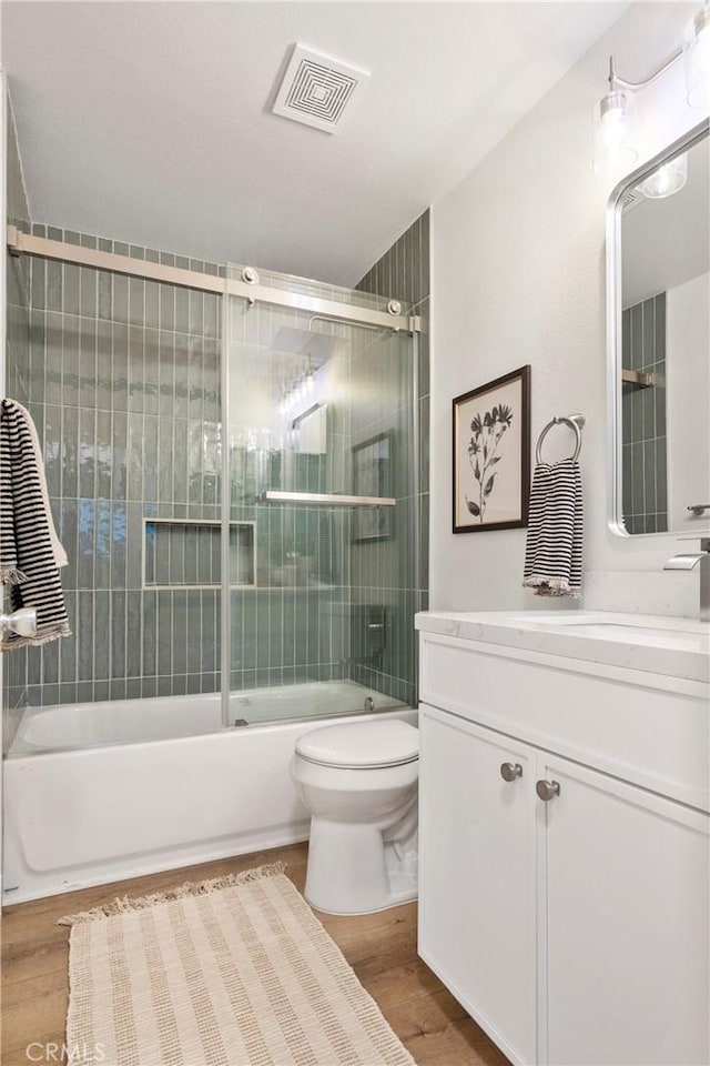 full bathroom featuring combined bath / shower with glass door, hardwood / wood-style floors, vanity, and toilet