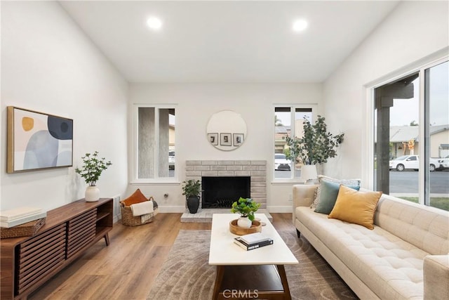 living room with vaulted ceiling, hardwood / wood-style flooring, and a brick fireplace