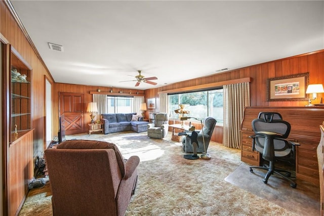 living room with carpet flooring, ceiling fan, crown molding, and wooden walls