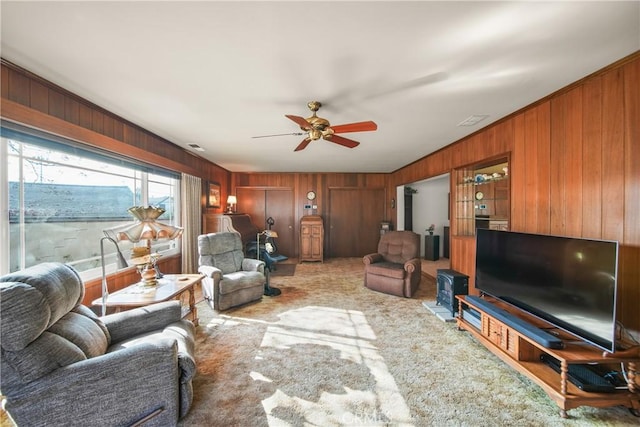 living room featuring wooden walls, ceiling fan, and light colored carpet