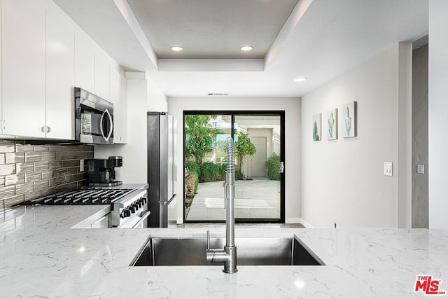 kitchen featuring decorative backsplash, light stone countertops, stainless steel appliances, sink, and white cabinets