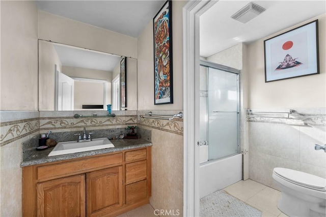 full bathroom featuring toilet, bath / shower combo with glass door, tile patterned flooring, tile walls, and vanity