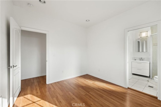 unfurnished bedroom with ensuite bathroom and light wood-type flooring