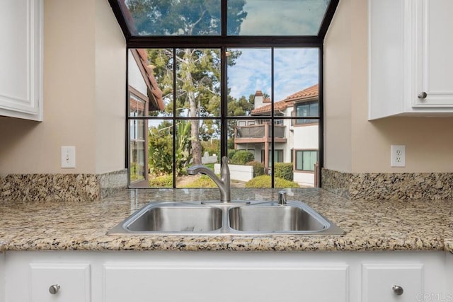 kitchen featuring light stone countertops, sink, and white cabinetry