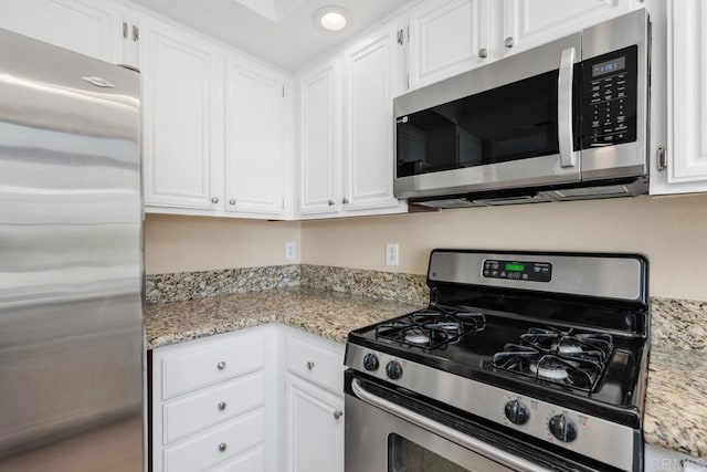 kitchen featuring stainless steel appliances, white cabinets, and light stone counters