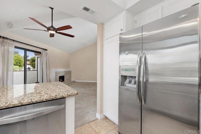 kitchen with light carpet, stainless steel appliances, vaulted ceiling, white cabinets, and light stone counters