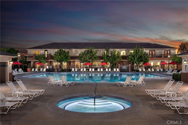 pool at dusk featuring a patio area and a hot tub